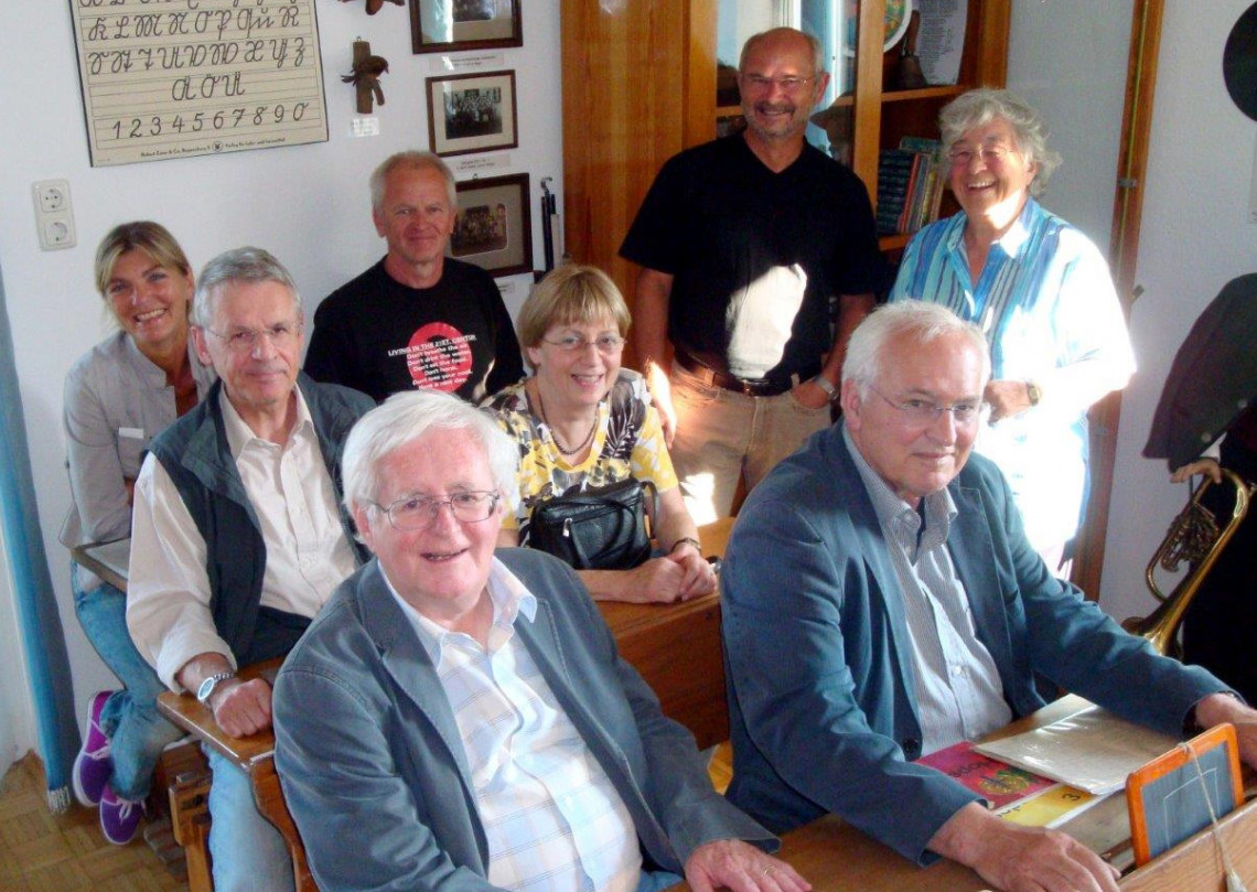 Erwachsene Museumsbesucher sitzen in den alten "erstklassler" Schulbänken